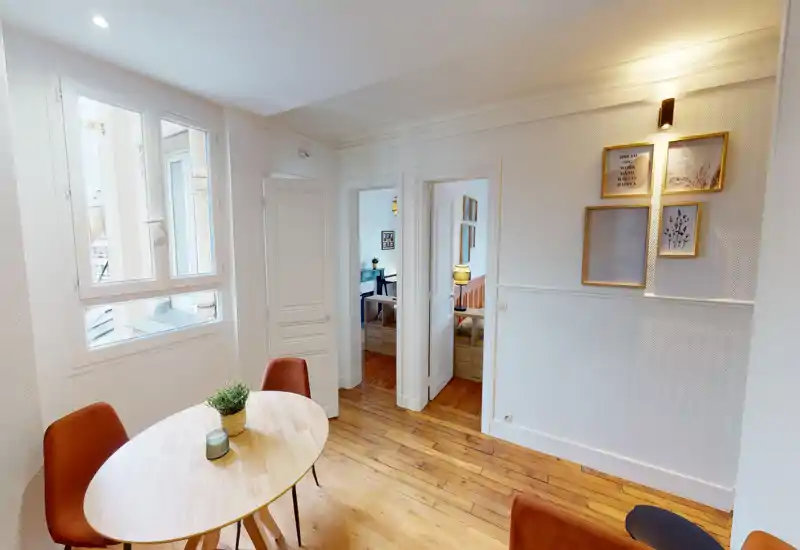 Coin repas compact et lumineux avec une table ronde en bois, chaises chaleureuses et lumière naturelle provenant d'une grande fenêtre — idéal pour des repas décontractés.
