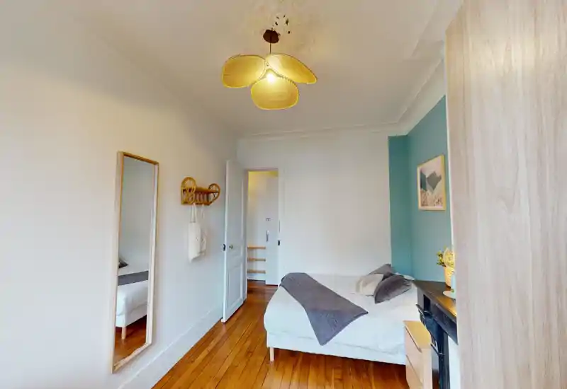 Camera da letto luminosa e curata con letto matrimoniale, biancheria morbida, cuscini decorativi e pavimenti in legno caldo che creano un'atmosfera accogliente.