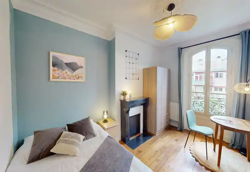 Camera da letto luminosa e ben arredata con comodo letto matrimoniale, lampada da comodino, armadio e una zona pranzo/scrittura vicino alla finestra ad arco che illumina l'ambiente.