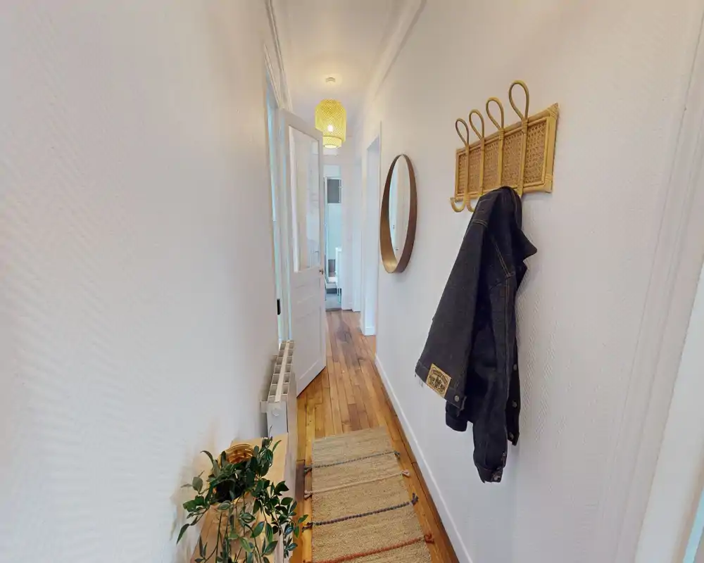 Entrée lumineuse et étroite avec sol en bois, patères murales et miroir rond — une première impression accueillante pour une location.
