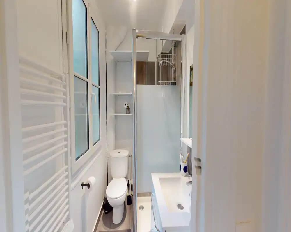 Salle de bains moderne et lumineuse avec cabine de douche, WC et lavabo dans un agencement compact. Finitions blanches et verre dépoli pour une impression de propreté.