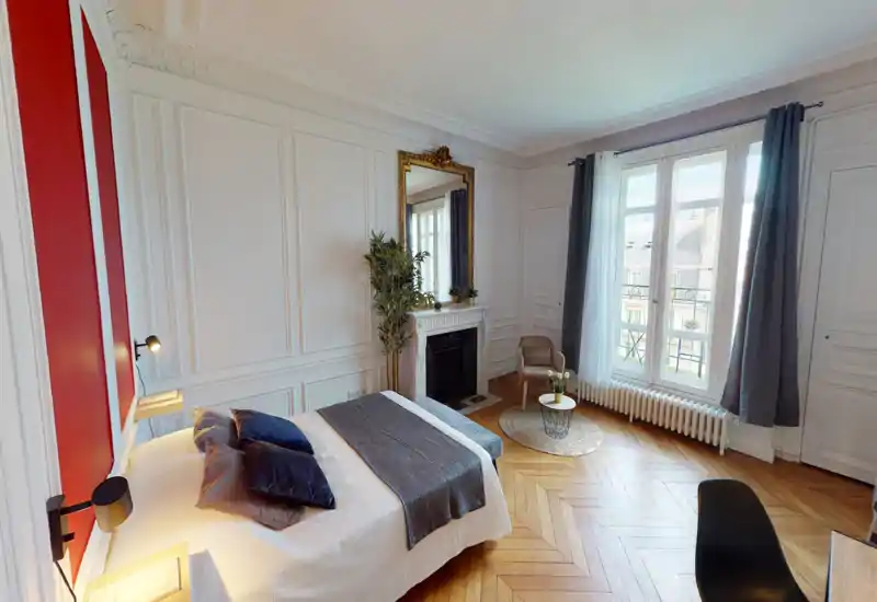Ampia camera da letto luminosa con pavimento in parquet, letto matrimoniale ben rifatto, modanature decorative e una grande finestra che illumina l'ambiente.