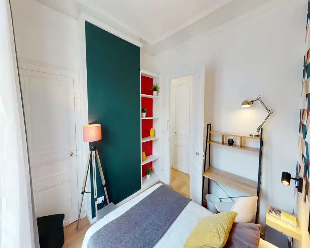 Chambre lumineuse et stylée avec lit double visible, coussins décoratifs et bureau avec lampe — décoration chaleureuse et contemporaine avec étagères intégrées.