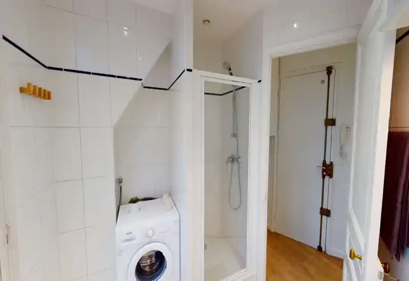 Salle de bain carrelée compacte avec cabine de douche et machine à laver ; carreaux blancs et équipements soignés pour un espace propre et fonctionnel.