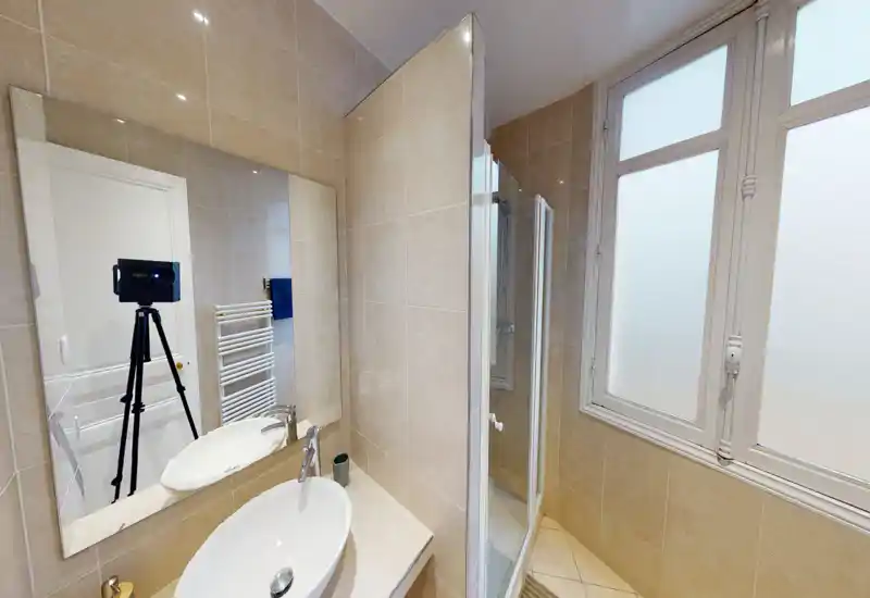 Salle de bain propre et lumineuse avec vasque sur plan, grand miroir et douche fermée à côté d'une fenêtre dépoli.