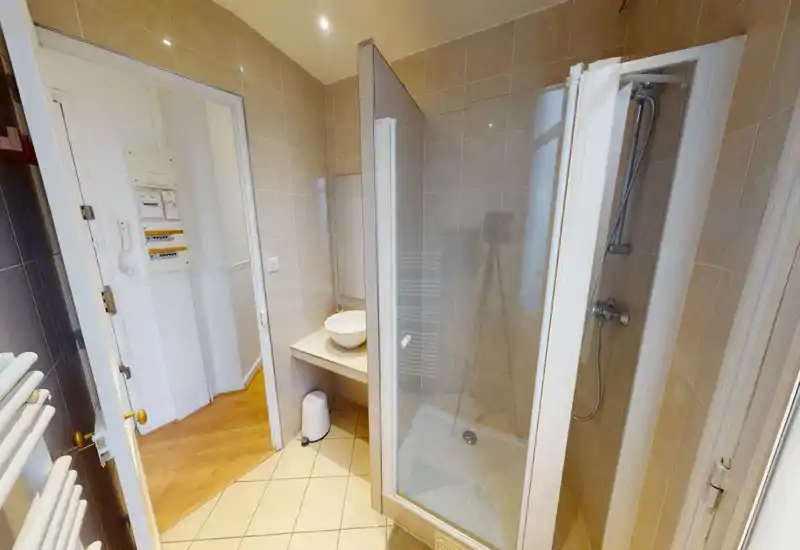 Salle de bains compacte carrelée avec douche d'angle vitrée, lavabo bol sur plan et éclairage chaud. Finitions modernes et propres, adapté aux courts séjours.
