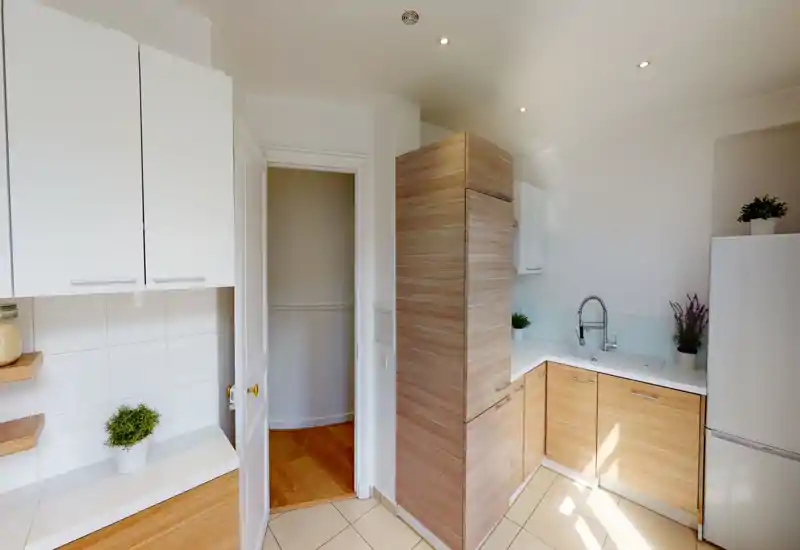 Cuisine moderne et lumineuse avec placards en bois clair, plans de travail blancs et électroménagers intégrés ; lignes épurées et petites plantes pour une atmosphère accueillante.