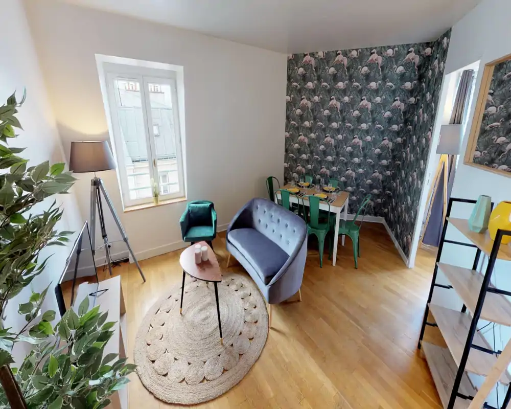 Salon lumineux et stylé avec canapé deux places en velours, fauteuil, tapis et petite table basse ; coin repas avec mur à motifs et chaises métalliques qui apportent du caractère.