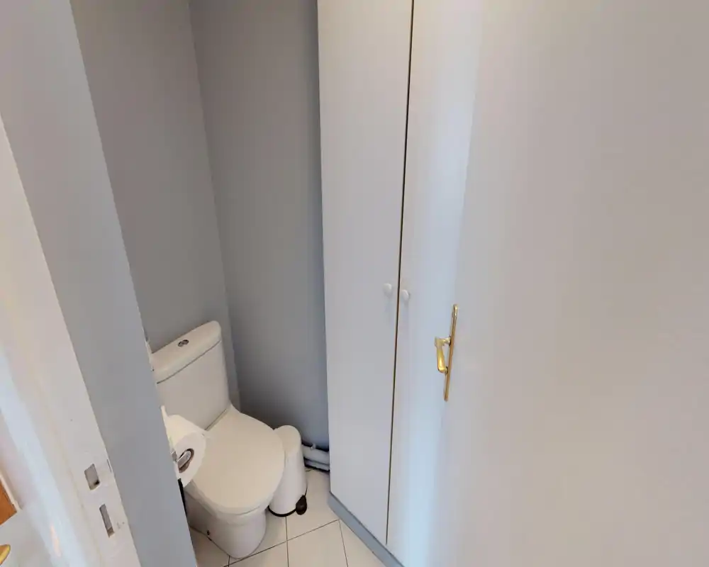 Petite salle d'eau avec WC moderne, sol carrelé et armoire de rangement blanche — propre et bien éclairée.