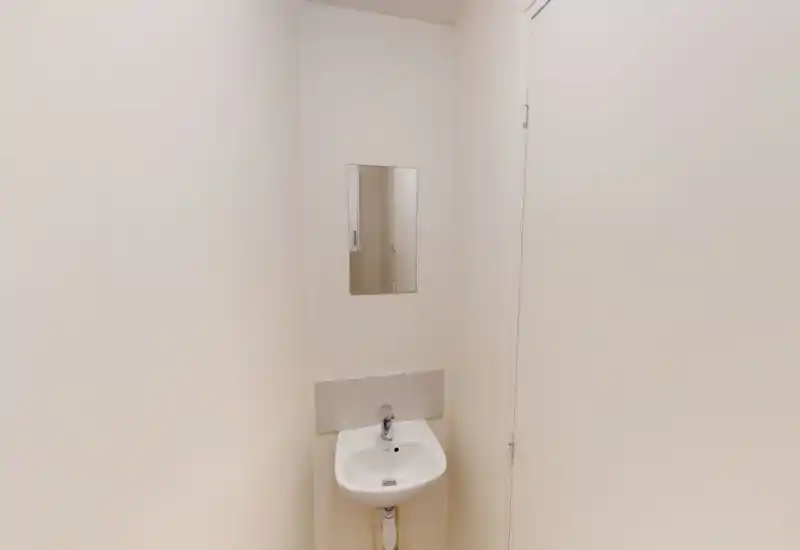 Small bathroom corner with a wall-mounted sink and a mirror above. The space is clean and simply finished with neutral walls and good lighting.