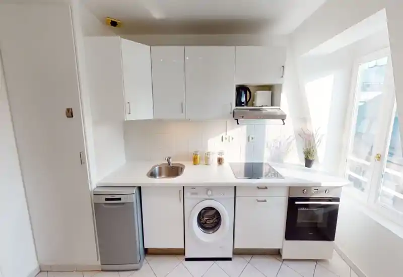 Bright, modern kitchenette with white cabinets, an induction hob, built-in oven and washing machine — ideal for compact urban living.