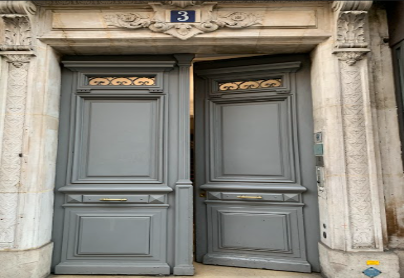 Grand painted double entrance door set in an ornate stone frame, with decorative panels and brass handles — a classic building entry.