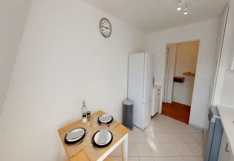 Compact, bright kitchen with a small dining table set for four, a refrigerator, and clean white finishes — ideal for a cozy city apartment.