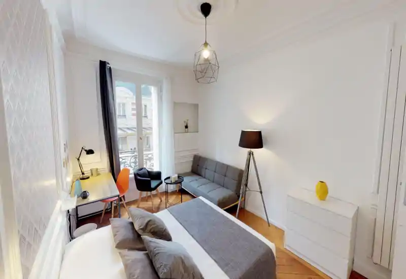 Bright, stylish bedroom with a comfortable double bed, a desk by the window, a compact sofa and tasteful lighting — ideal for short-term rentals.