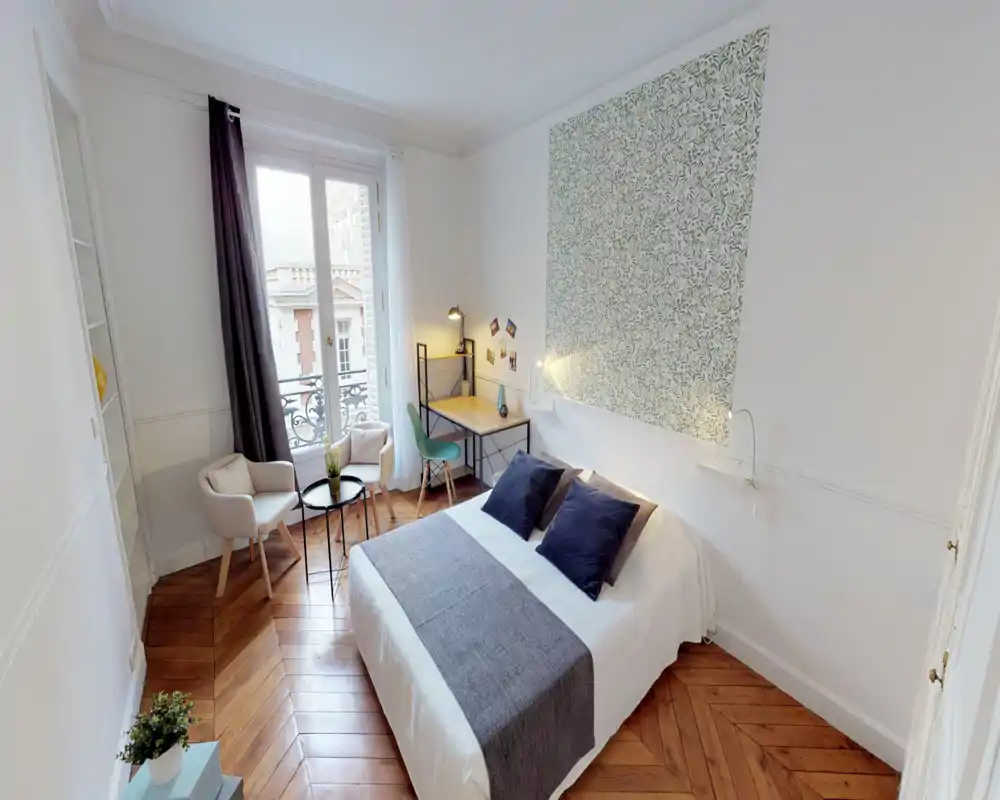 Chambre lumineuse et élégante avec lit double, papier peint décoratif, petit coin salon et bureau près de la fenêtre—parfaite pour un séjour confortable.