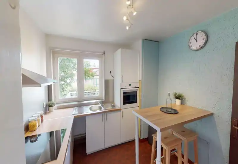 Compact kitchen area with light cabinetry, countertop and window light; modest decorative touches provide a homely feel despite image artifacts.