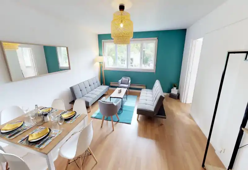 Bright, modern living room with sofas, a coffee table and large windows providing natural light. The teal accent wall and layered textiles create a welcoming seating area.