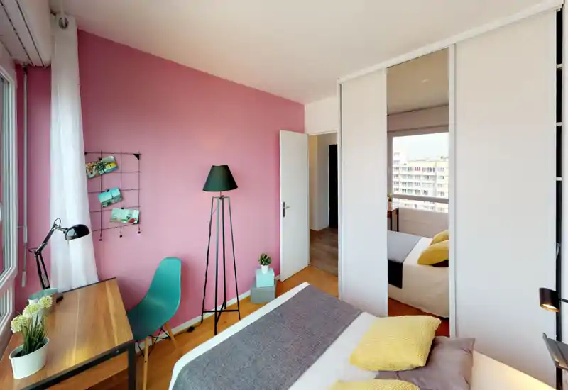 A bright, stylish bedroom with a comfortable double bed, cozy pillows and warm textiles. Natural light from the large window and a mirrored wardrobe add depth, while a small desk and lamp create a versatile workspace.
