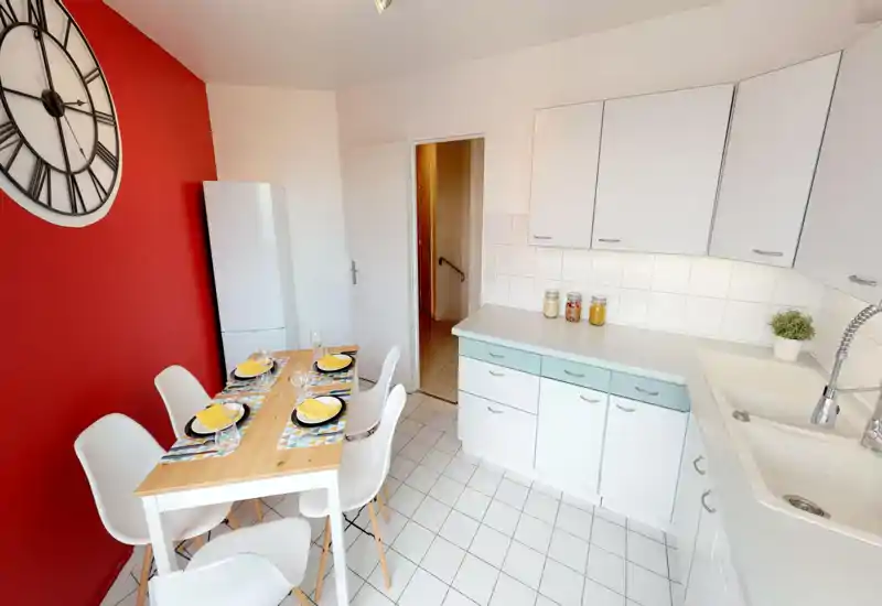 Bright, modern kitchen with a small dining table set for four. White cabinets, tiled floor and a bold red accent wall create a fresh, inviting space ideal for casual meals.