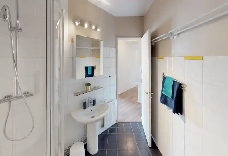 Bright, modern bathroom with a standing sink, wall-mounted mirror cabinet, towel rails and a shower enclosure. Clean white tiles and dark floor create a fresh contrast.