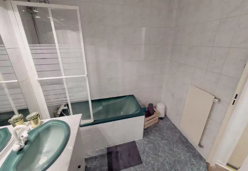Compact tiled bathroom with a green sink and matching bathtub, glass shower screen, wall-mounted radiator and tiled floor — neat and functional.