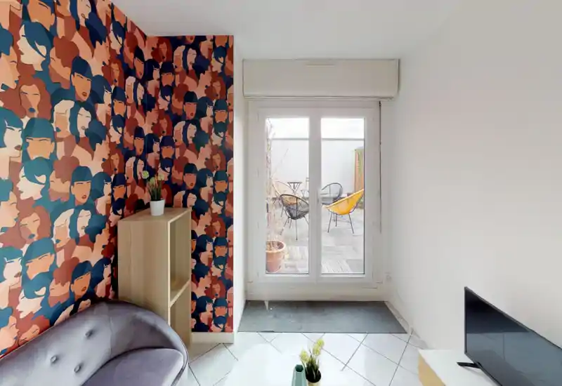 Compact, stylish living area with a patterned accent wall, small sofa, TV and a glass door opening to a sunny terrace — bright and inviting for relaxing or entertaining.