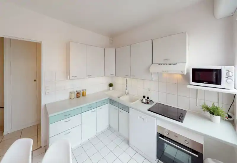 Bright and tidy compact kitchen with white cabinets, integrated oven, induction hob and microwave. Clean tiled backsplash and practical countertop space, ideal for efficient cooking.