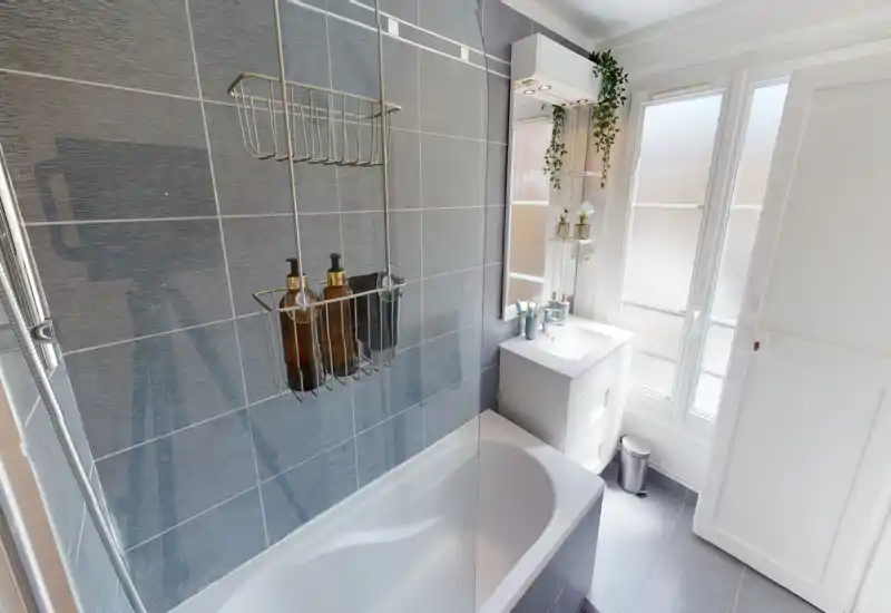 Bright, modern bathroom with a bathtub and wall-mounted shower caddy, white vanity and frosted windows letting in natural light.