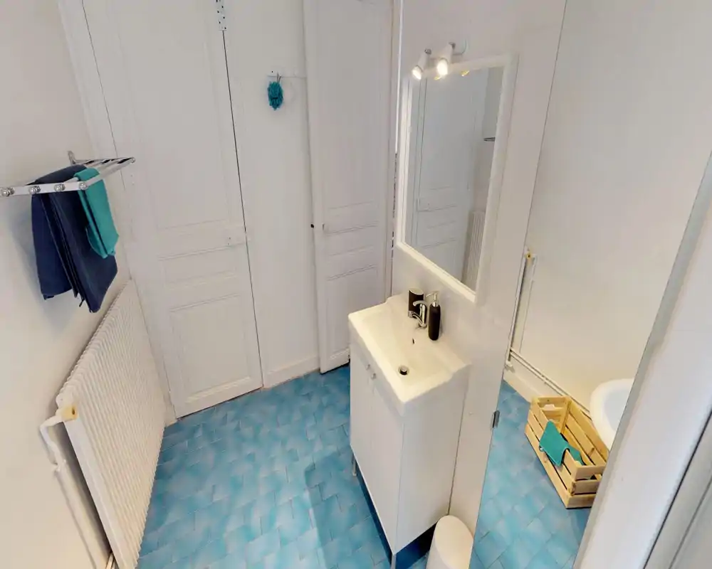 Bright, compact bathroom with a white vanity and mirror, blue tiled floor and simple accessories. Clean, functional layout ideal for short stays.