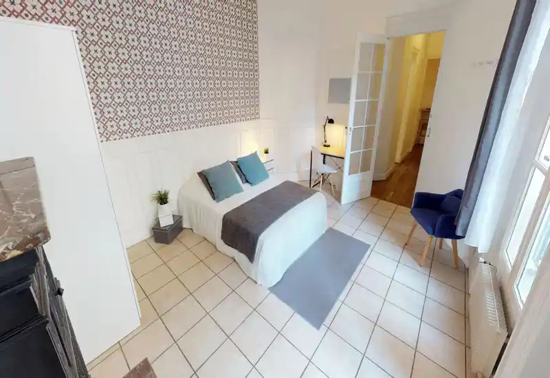 Bright, well-staged bedroom with a double bed, decorative cushions, a bedside lamp and a small desk by the door. Patterned accent wall and tiled floor add character while large window brings natural light.
