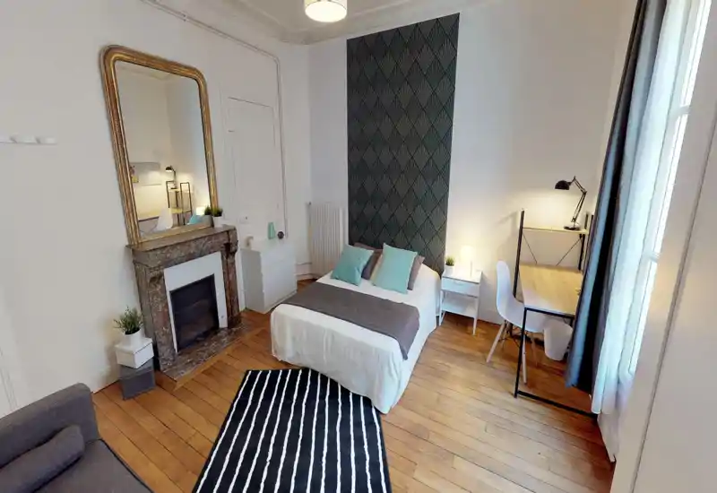 Bright, stylish bedroom with a centrally placed double bed, decorative wallpaper behind the headboard, bedside tables with lamps and a desk by the window — ideal for comfortable stays and remote work.