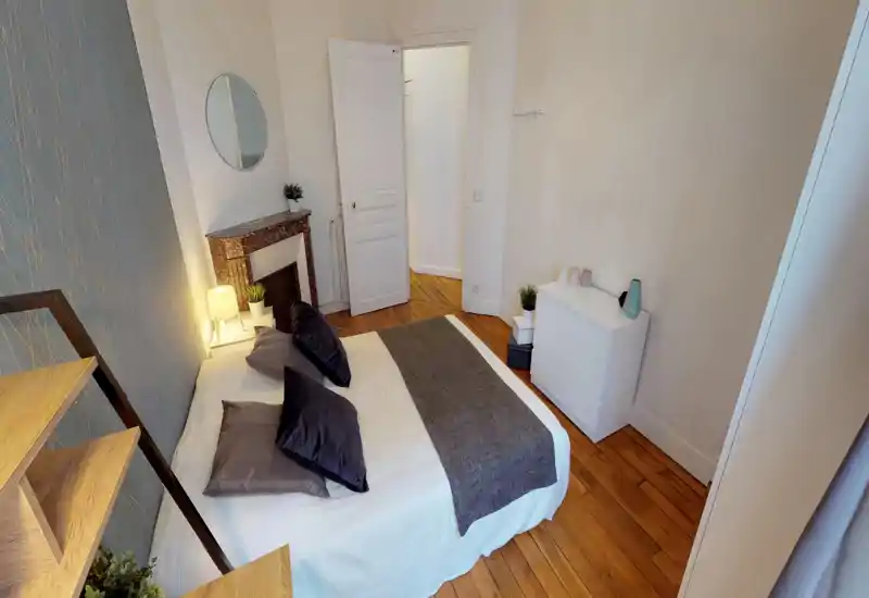 Bright, well-styled bedroom with a double bed, soft linens, decorative pillows and a bedside lamp; wooden floors and a white chest of drawers complete the cozy layout.