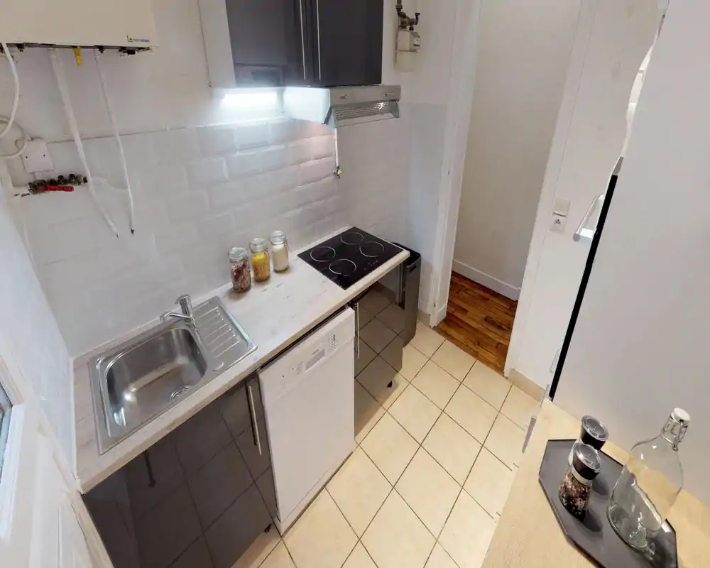 Compact modern kitchen with a stainless sink, induction hob and built-in dishwasher. White tiled backsplash and light wood countertop create a clean, practical workspace.