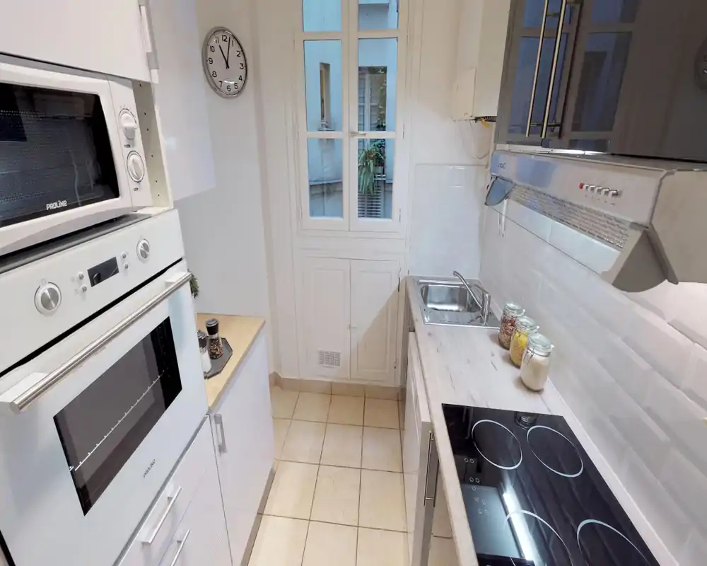 Compact modern kitchen with built-in oven, electric cooktop and stainless sink; light wood counters and white subway-tile backsplash create a bright, clean cooking space.