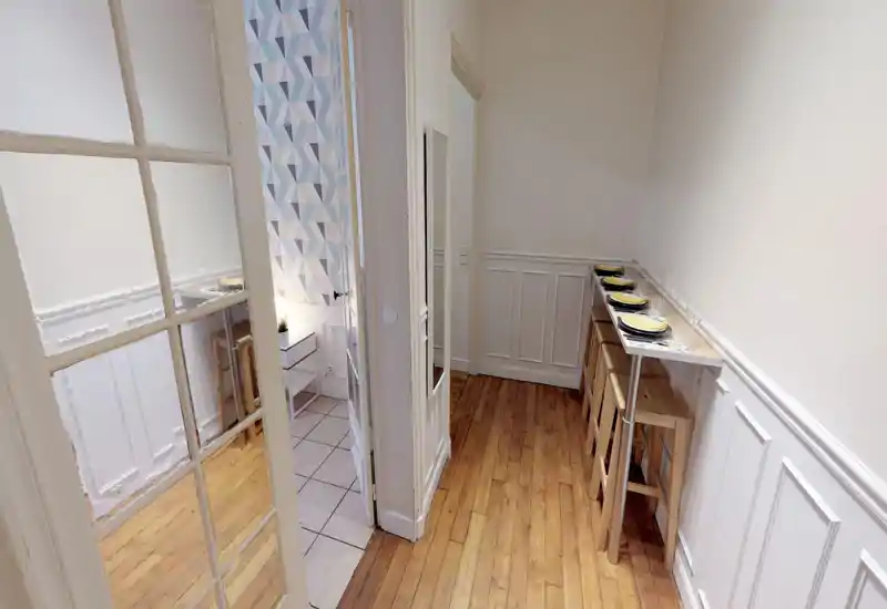 Narrow dining area with a high counter and wooden stools set for multiple guests; bright, minimalist décor and parquet floors create a clean, modern feel.