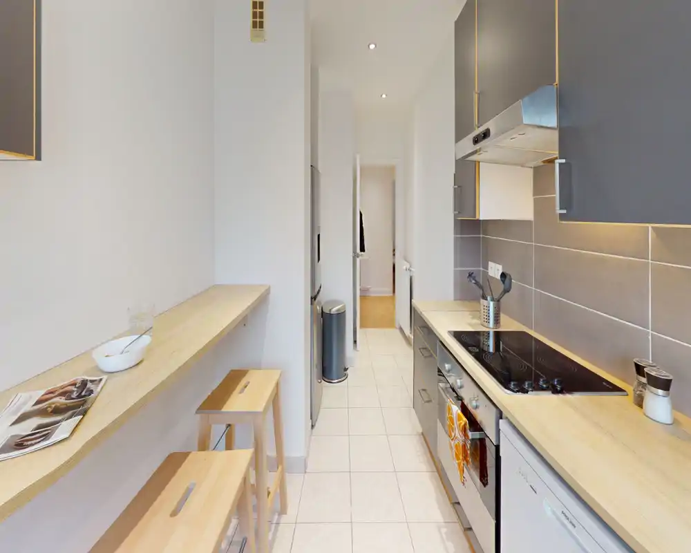 Cuisine en enfilade moderne et lumineuse avec plans de travail en bois, placards gris, four encastré et plaque vitrocéramique — un espace compact et bien organisé, parfait pour un appartement en ville.