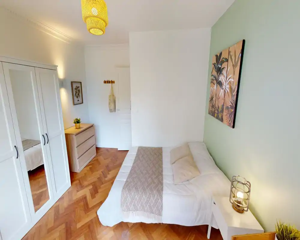 Bright, well-styled bedroom with a comfortable double bed, decorative throw and cushions, wooden parquet flooring and a white wardrobe with mirrored doors.