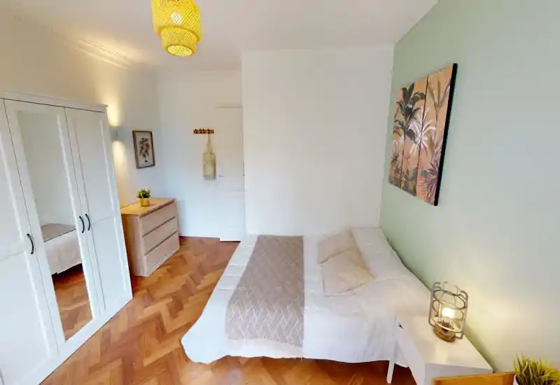 Bright, well-styled bedroom with a comfortable double bed, decorative throw and cushions, wooden parquet flooring and a white wardrobe with mirrored doors.