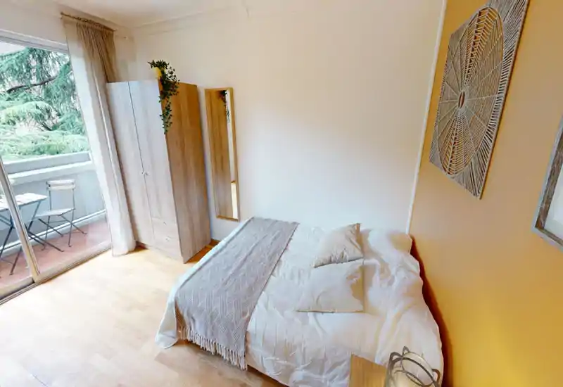 Camera da letto luminosa e accogliente con letto matrimoniale in tessili neutri, armadio in legno, specchio a figura intera e balcone con sedute esterne visibile tramite porte scorrevoli.