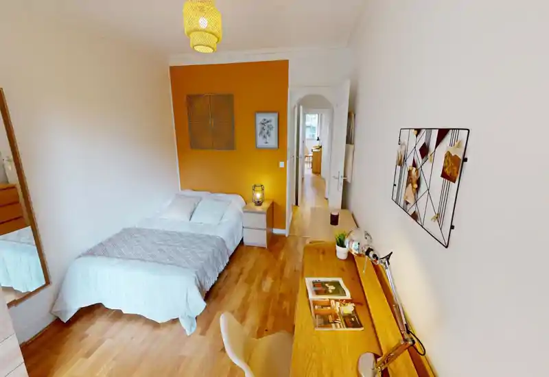 Camera da letto luminosa e ben arredata con un comodo letto matrimoniale contro una parete color ocra, comodino con lampada e una scrivania in legno adatta al lavoro o alla lettura.