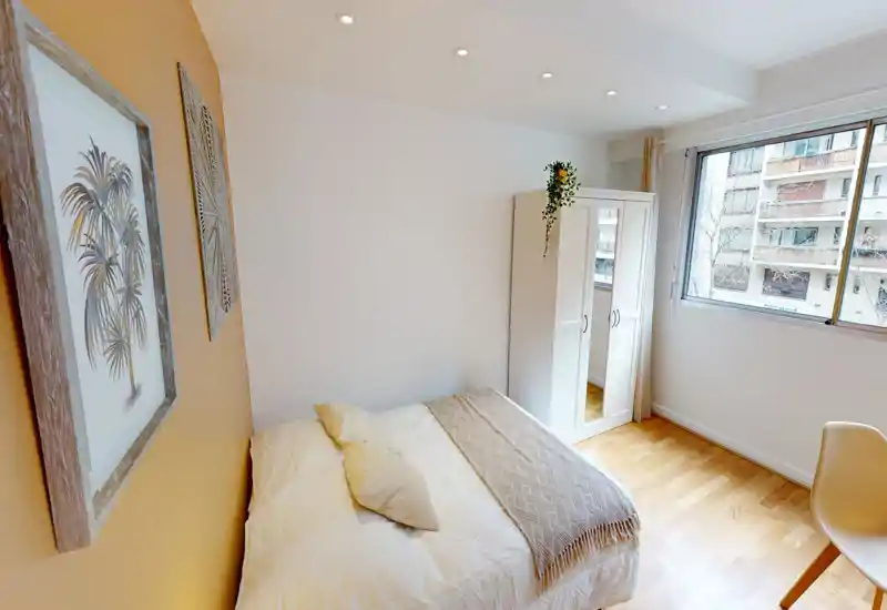 Bright, cozy bedroom with a double bed, soft linens, a textured throw and a wardrobe beside a large window that fills the room with natural light.