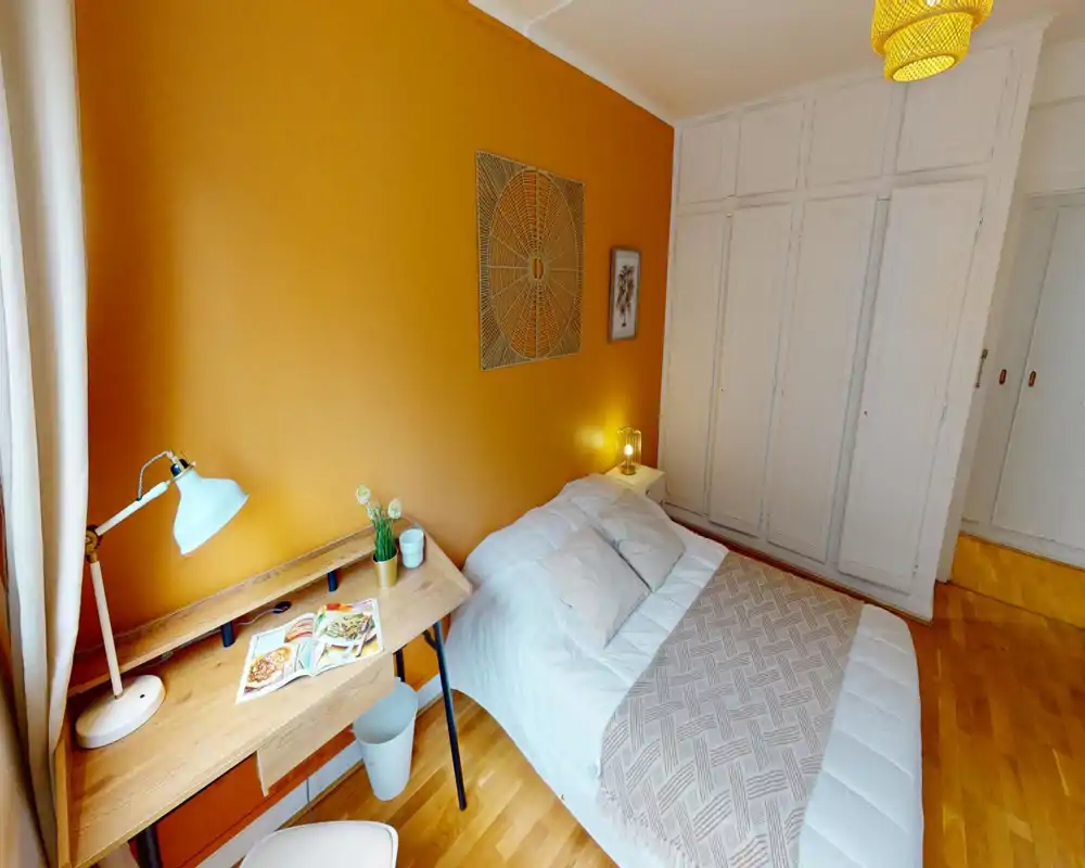 Chambre chaleureuse et soignée avec lit double, table de chevet et grands placards blancs intégrés. Le mur orange et les textiles doux donnent une ambiance cosy, idéale pour une annonce locative.