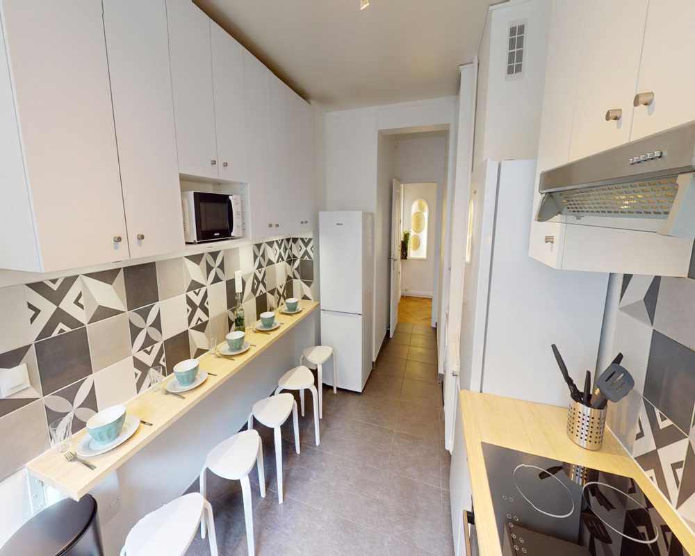 Compact modern kitchen with a patterned tile backsplash, integrated cabinets, breakfast bar and stools — bright, well organized and ideal for casual dining.