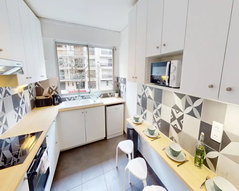 Bright, modern kitchen with patterned tile backsplash, wooden countertops, integrated oven and microwave, and a small breakfast bar — ideal for compact city apartments.