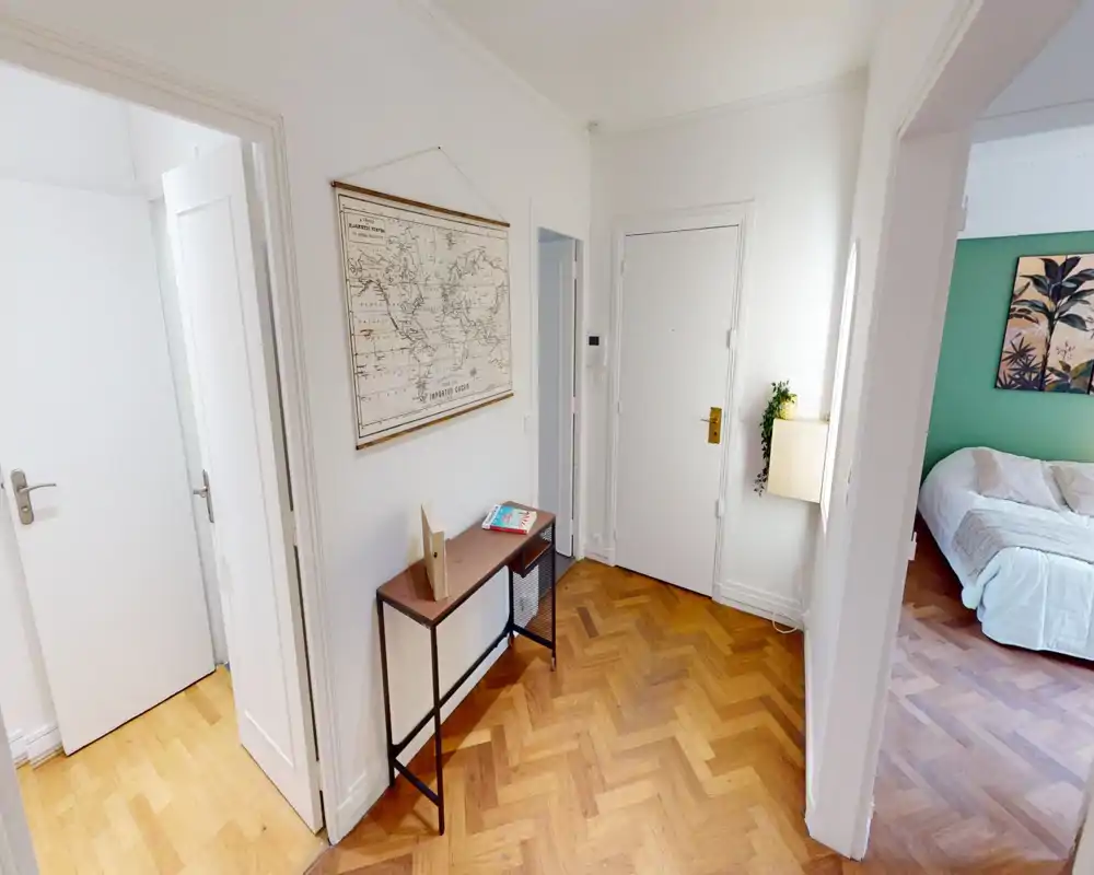 Bright, welcoming entrance hall with a console table, decorative map on the wall and parquet flooring; view into an adjacent bedroom.