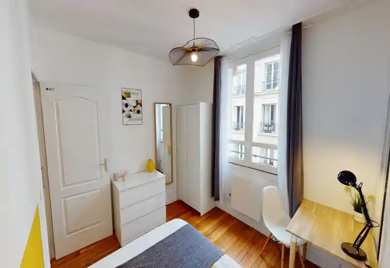Bright, compact bedroom with natural light, a visible double bed, wooden floors and a small workspace by the window — ideal for single or couple stays.