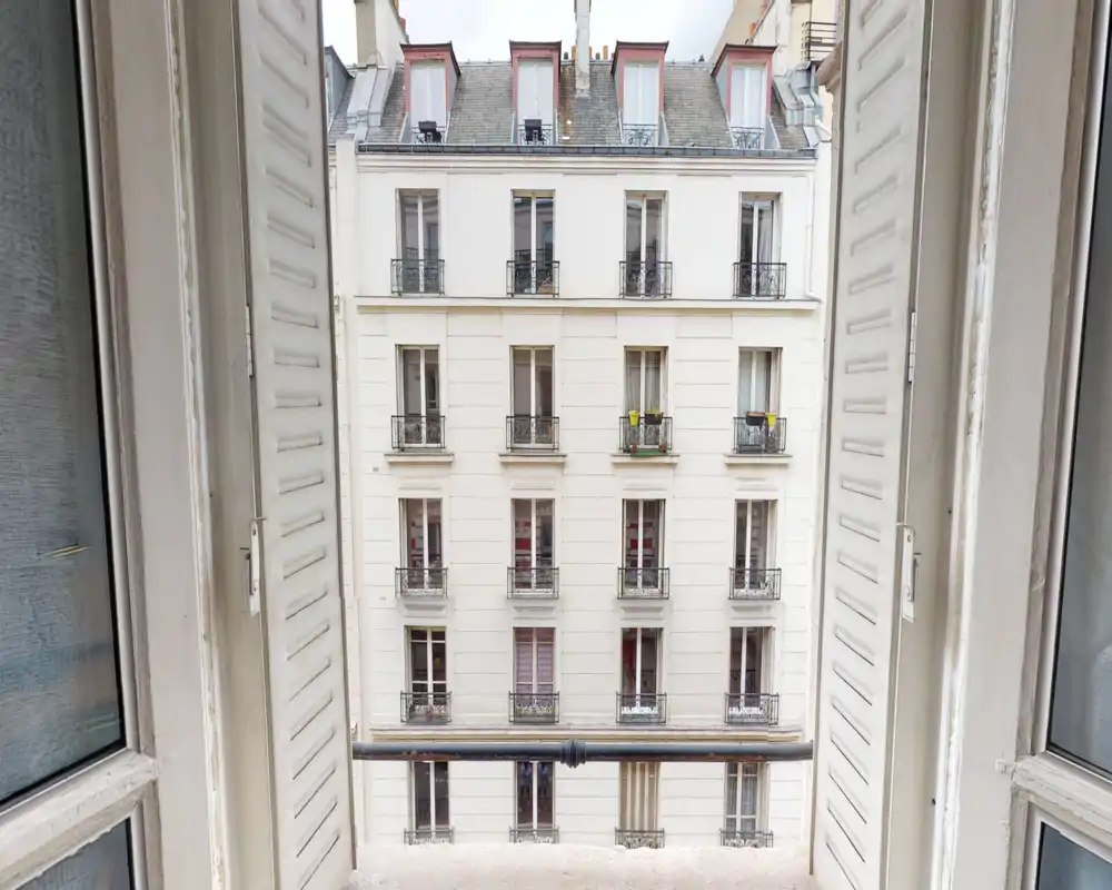 Open window framing an urban balcony/view: clear view of the neighboring building facade and small balcony rail, great for showing the external outlook of the apartment.