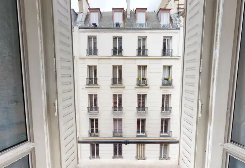 Open window framing an urban balcony/view: clear view of the neighboring building facade and small balcony rail, great for showing the external outlook of the apartment.