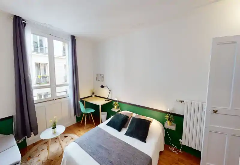 Bright, styled bedroom with a double bed, cozy textiles and a small desk by the window. Natural light and green accents create a welcoming atmosphere ideal for short stays.