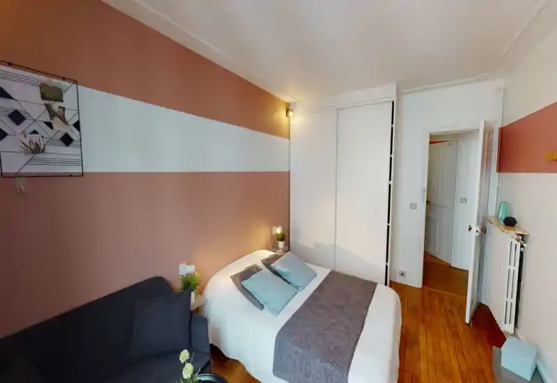 Camera da letto luminosa e curata con letto matrimoniale, cuscini morbidi e plaid; parete accentata rosa e armadio a muro che rendono l'ambiente accogliente.